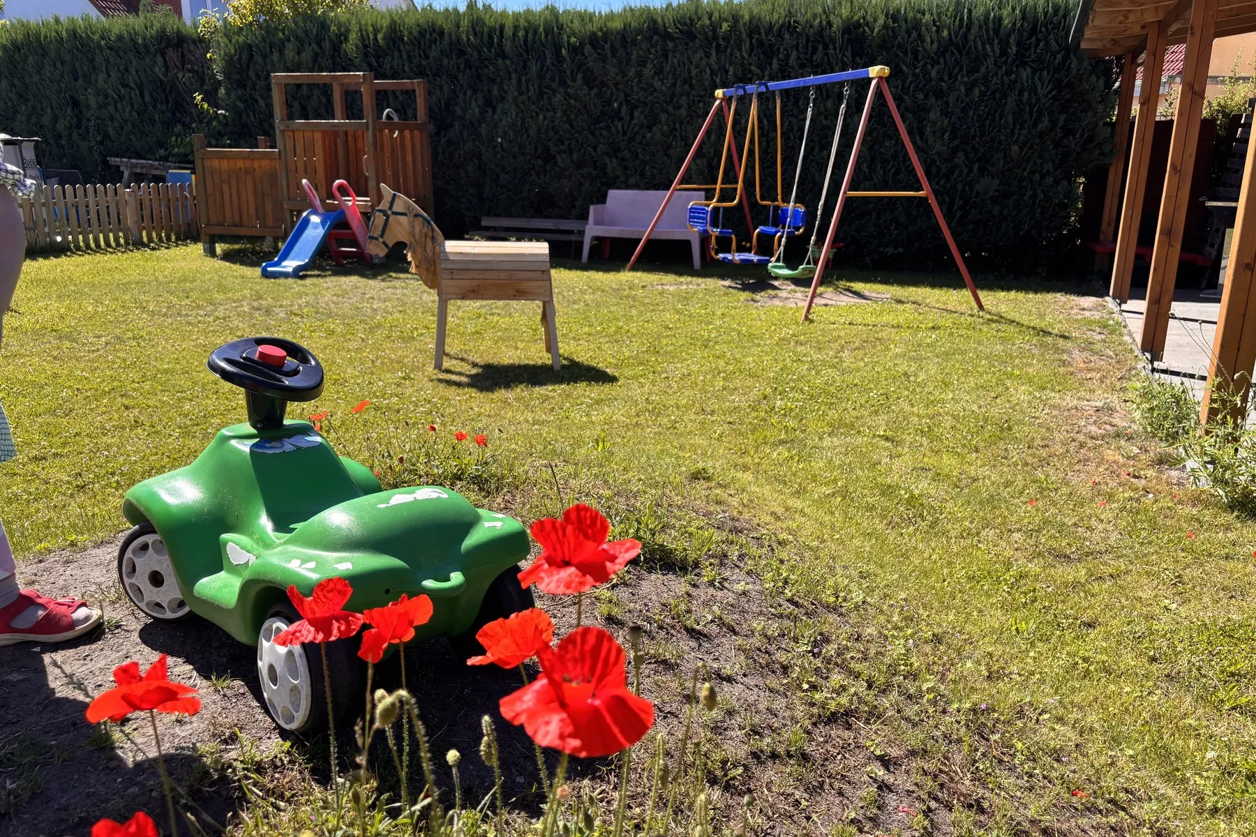 Garten mit Schaukelgerüst, hölzernem Spielpferd und einem grünen Rutschauto