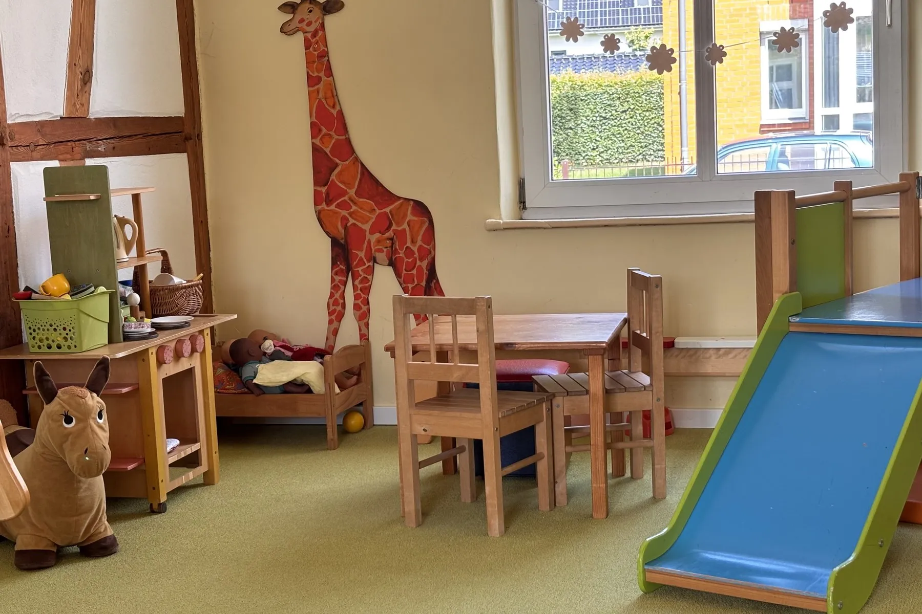 Essbereich mit Kindertisch und Holzstühlen, an der Wand eine große gemalte Giraffe